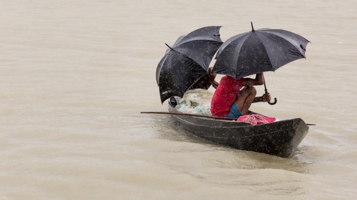 Men in a wooden canoe sheltering under umbrellas from the monsoon rain, in Bangladesh.