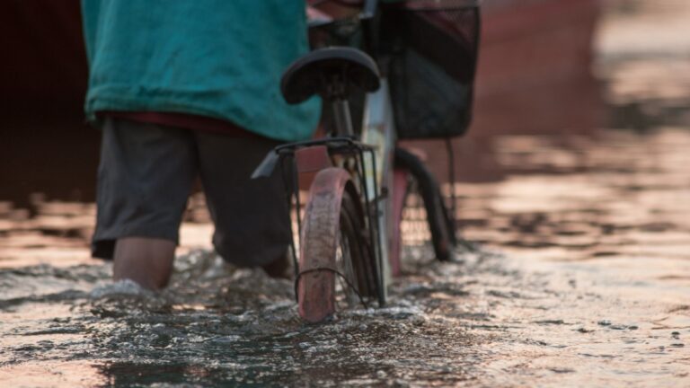 A person walks their bike through a knee-level flood.