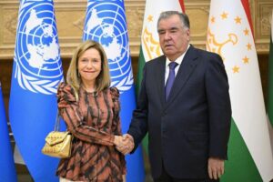 Celeste Saulo, secretary-general of the World Meteorological Organization, and Emomali Rahmon, President of Tajikistan shake hands in front of four flags.