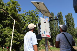 Two users look up at a weather monitoring station with solar panel.
