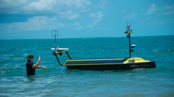 A woman points to a yellow uncrewed surface vessel in the sea.