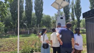 A group of five people look up at a weather monitoring station with solar panel.