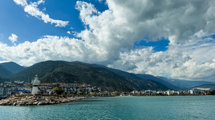 A lighthouse looks out on a turquoise ocean and building clouds.