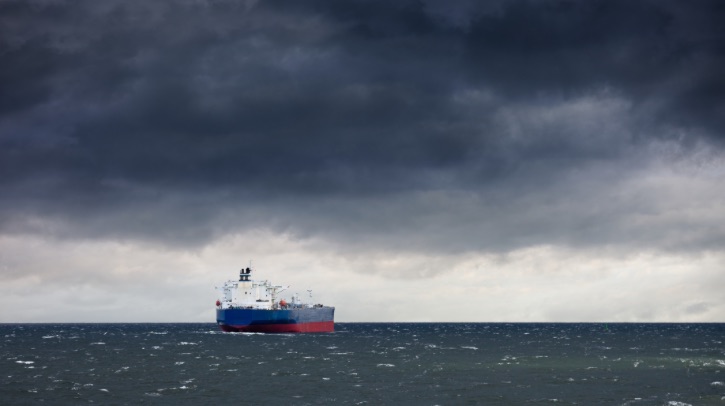 A ship sails across the sea, toward a dark cloudy stormy sky.