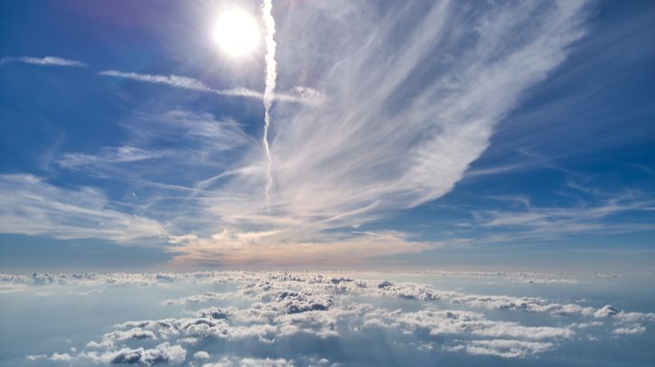 A picture taken at altitude of clouds in the sky and the sun above looking out towards space