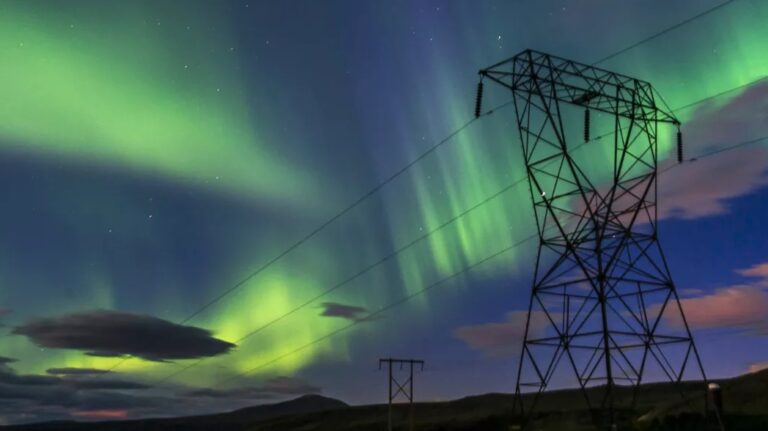 A magnetic storm of greens and pinks in the night sky view from the ground, with power lines cutting across the image