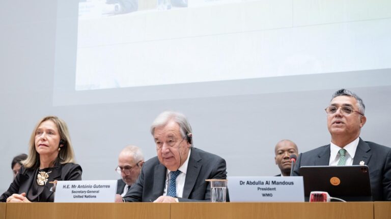 Prof. Celeste Saulo, WMO Secretary-General; António Guterres, Secretary-General of the United Nations; Dr Abdulla Al Mandous, WMO President sit at a desk at the WMO Extraordinary World Meteorological Congress meeting with a large projector screen behind them
