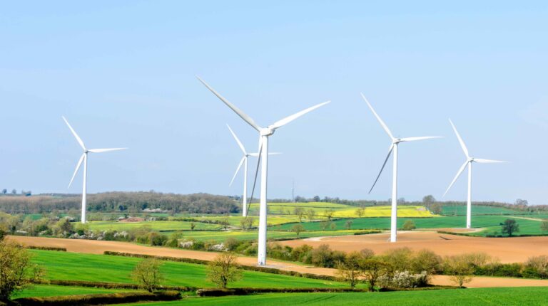 Three wind power turbines on a green field landscape