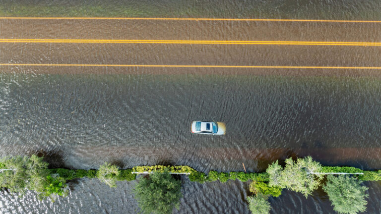 An aerial photo of a car submerged on an empty highway with trees lining the road through the water