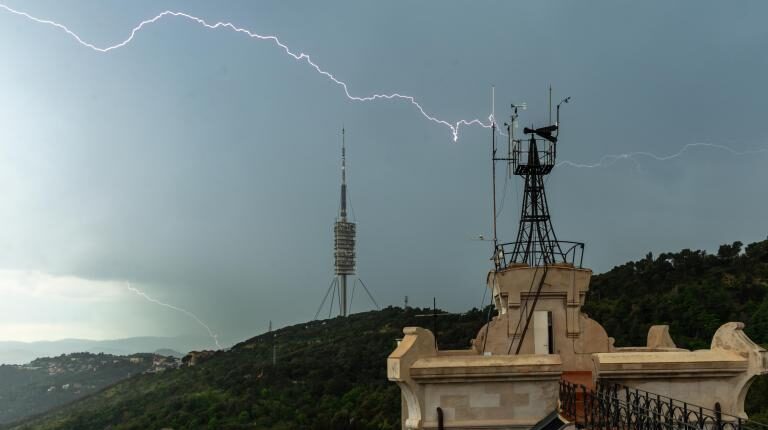 A storm moves over a hill, with lightning moving across the sky and a weather station in the foreground