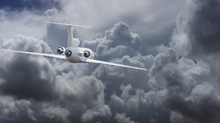 A twin-engine business jet flies towards dark grey storm clouds