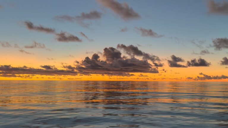 The sun sets behind a cloud over the sea