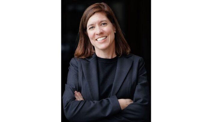 Profile photo of AMS executive director Amanda Staudt, who is standing with her arms crossed against a black background.