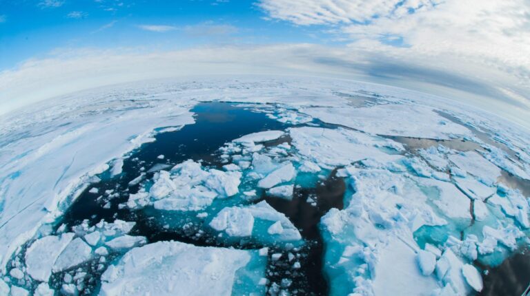 Arctic Ocean sea ice and ice floes breaking up and melting, depicting environment, global warming, and climate change impacts with dark water visible under a wide blue sky