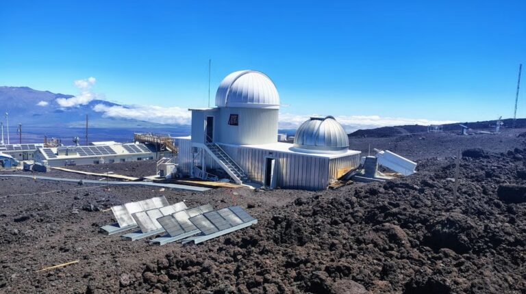 The Mauna Loa Solar Observatory stands on a hillside with a large blue sky above it.